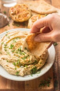 Hand Dipping Pita Bread into a Plate of Roasted Garlic Hummus