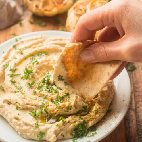 Hand Dipping Pita Bread into a Plate of Roasted Garlic Hummus