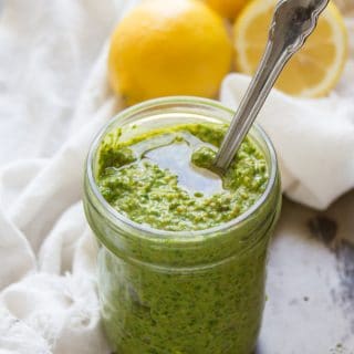 Jar of Vegan Pesto with a Spoon Inside and Lemons in the Background