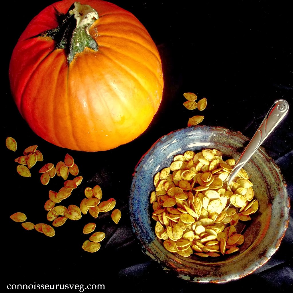 Overhead View of a Dish of Pumpkin Seeds with Spoon and Pumpkin on a Black Surface