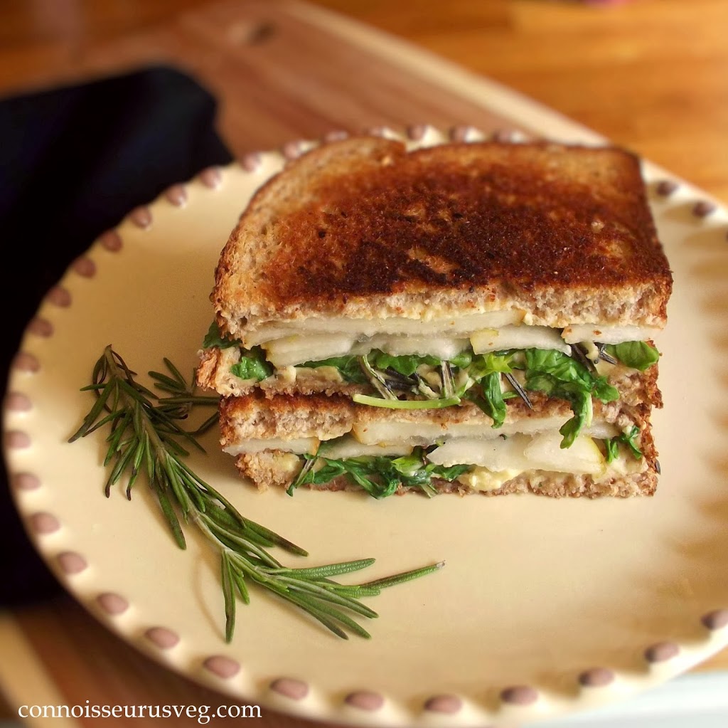 Two Halves of a Panini Stacked on a Plate with a Sprig of Rosemary