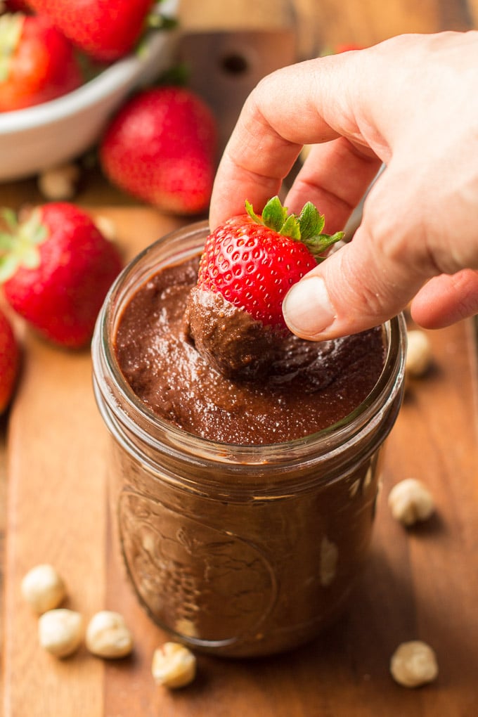 Hand Dipping a Strawberry into a Jar of Vegan Nutella
