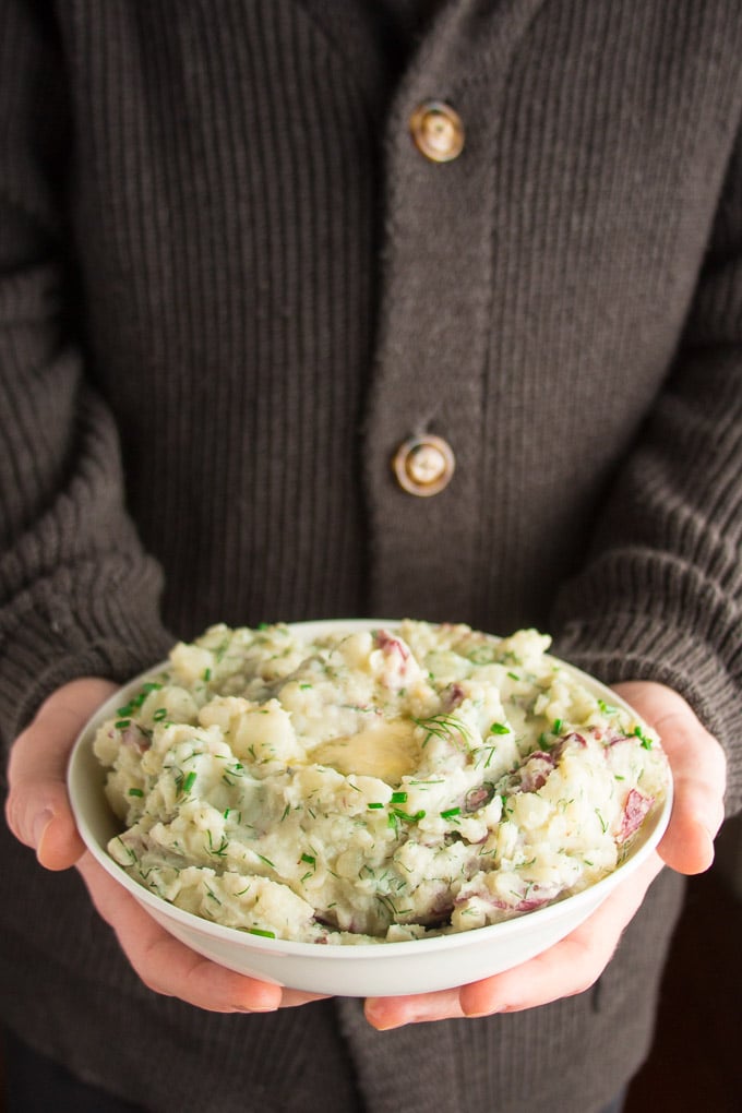 Pair of Hands Holding a Bowl of Mashed Red Potatoes with Roasted Garlic & Dill