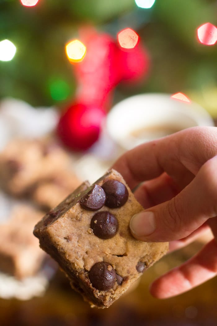 Close Up of a Hand Holding a Chocolate Chunk Cookie Butter Blondie, with Christmas Lights in the Background