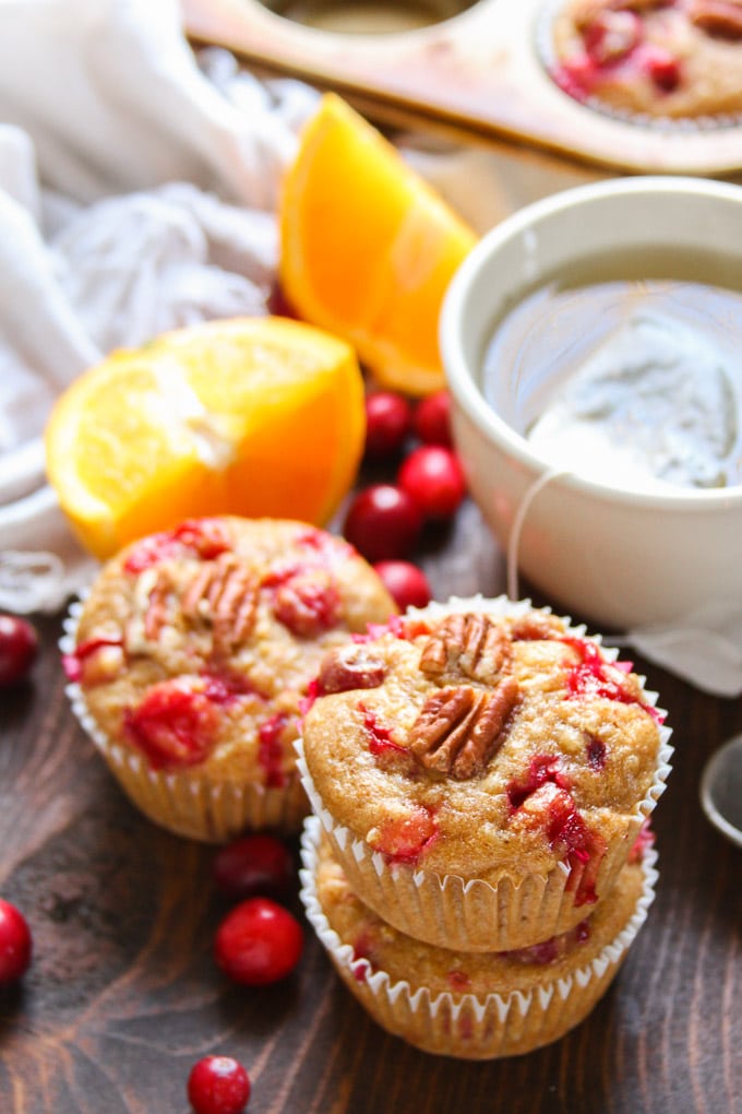 Stack of Two Cranberry Orange Quinoa Muffins with Another Muffin, Teacup and Orange Slices in the Background