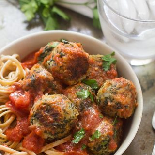 Bowl of Cannellini Bean & Broccoli Rabe Meatballs Over Linguine with Water Glass in the Background