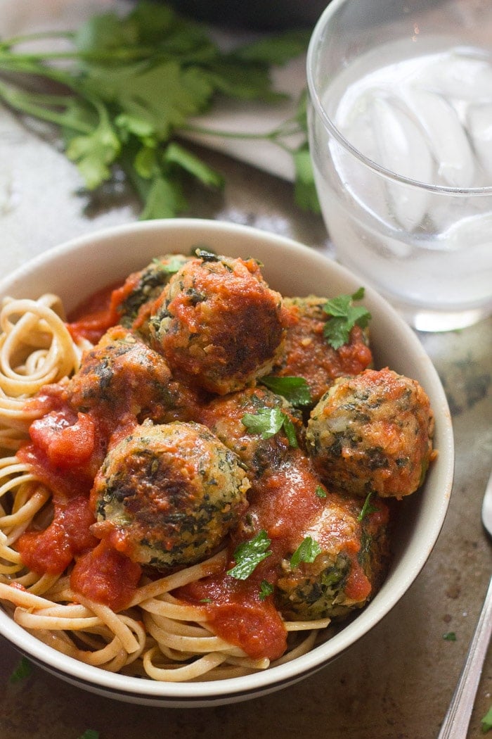 Bowl of Cannellini Bean & Broccoli Rabe Meatballs Over Linguine with Water Glass in the Background