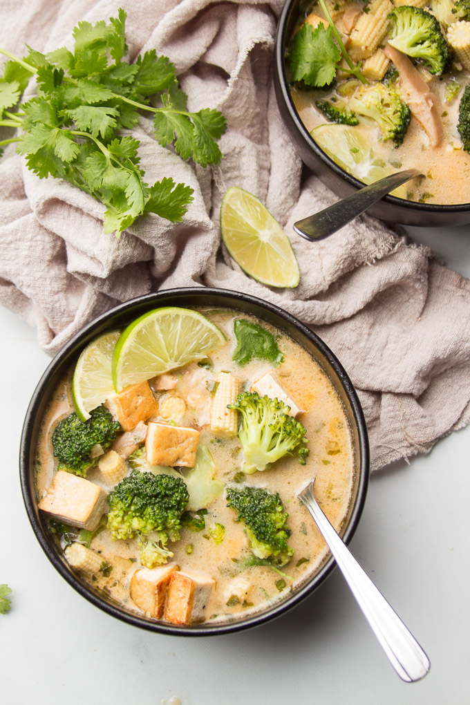 Two Bowls of Thai Coconut Soup with Lime Wedges and Spoons