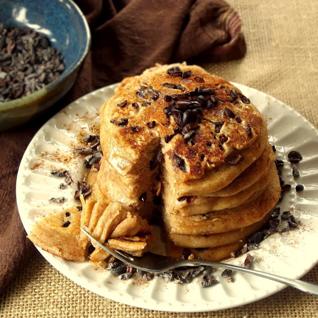 Stack of Pancakes on a Plate with Cacao Nibs on Top and a Wedge Cut Out and Held on a Fork