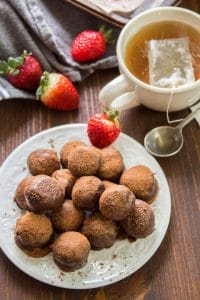 Plate of Vegan Truffles with Strawberries and a Cup of Tea in the Background