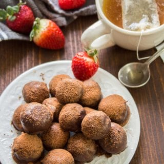 Plate of Vegan Truffles with Strawberries and a Cup of Tea in the Background