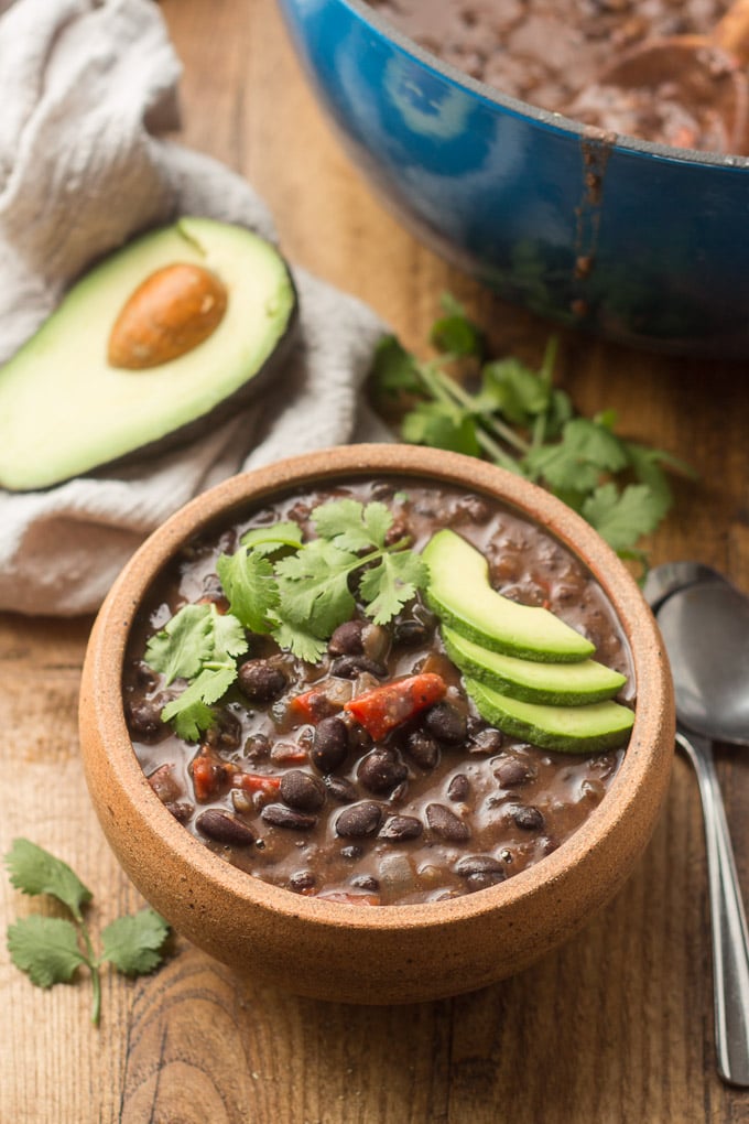 Spicy Black Bean Soup with Pot, Cilantro, Napkin and Avocado Half in the Background.