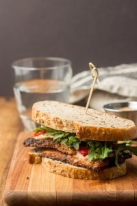 Blackened Tempeh Sandwich on a Cutting Board with Glass of Water in the Background