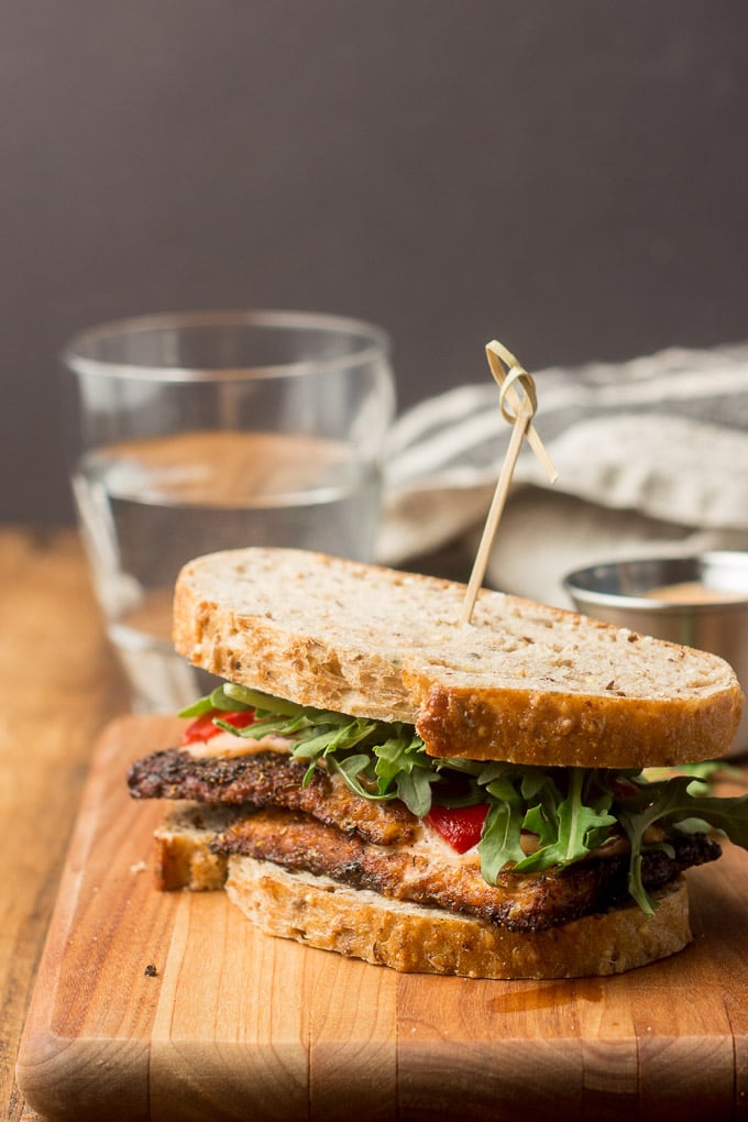Blackened Tempeh Sandwich on a Cutting Board with Glass of Water in the Background