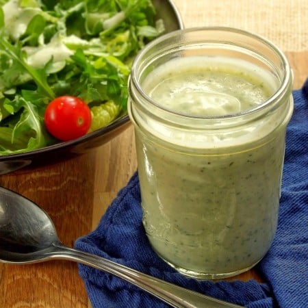 Jar of Vegan Ranch Dressing with Spoon in the Foreground and Bowl of Salad in the Background