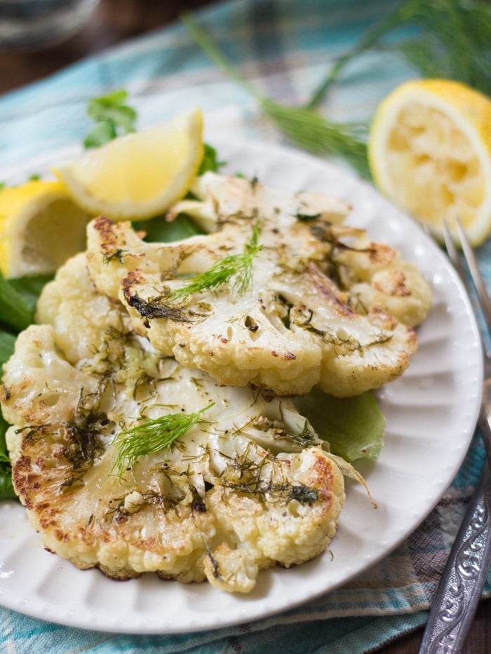 Close Up of Two Cauliflower Steaks on a Plate with Lemon Wedges