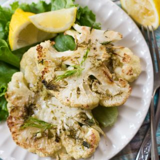 Overhead View of Two Cauliflower Steaks on a Plate with Lettuce and Lemon Wedges