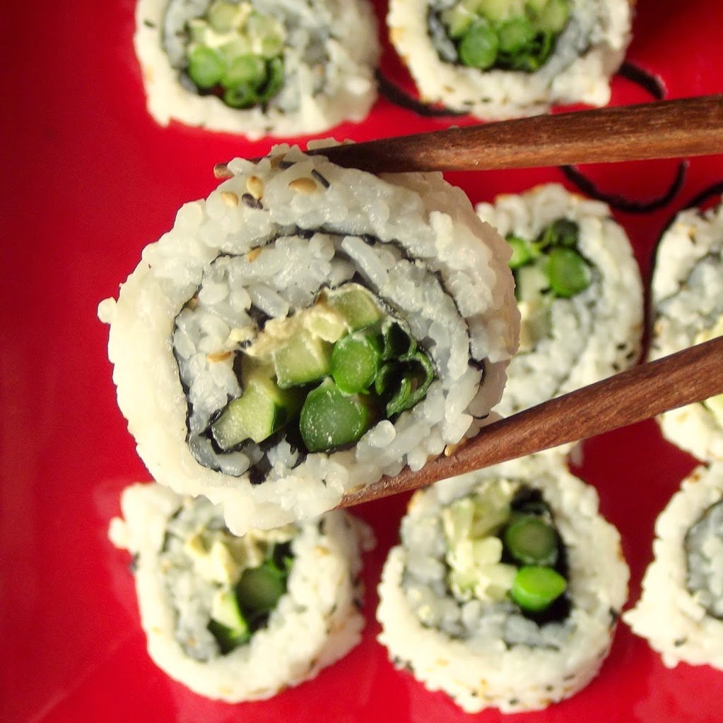 Close Up of a Pair of Chopsticks Holding a Piece of Veggie Sushi Over a Red Plate
