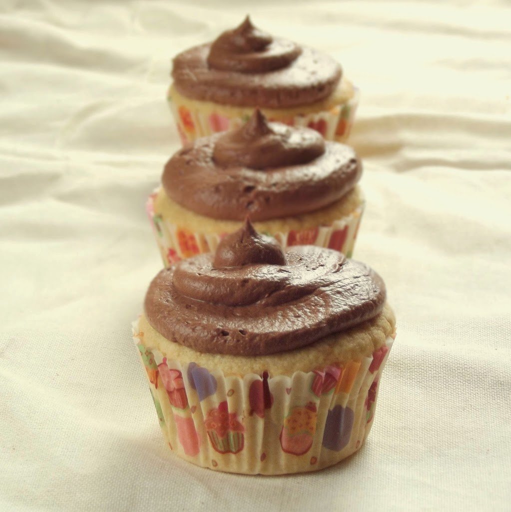 Row of Three Cupcakes with Chocolate Frosting on White Fabric