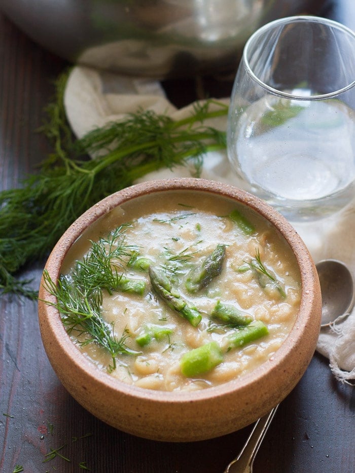 Bowl of Creamy White Bean Asparagus & Dill Soup with Pot and Water Glass in the Background