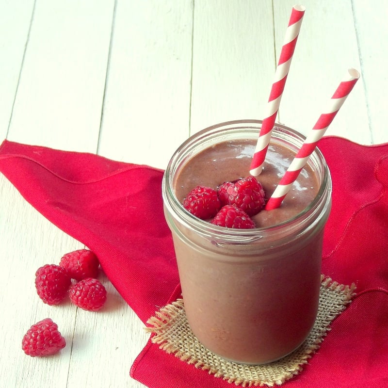 Chocolate Smoothie in a Glass with Two Straws and Fresh Raspberries on Top.