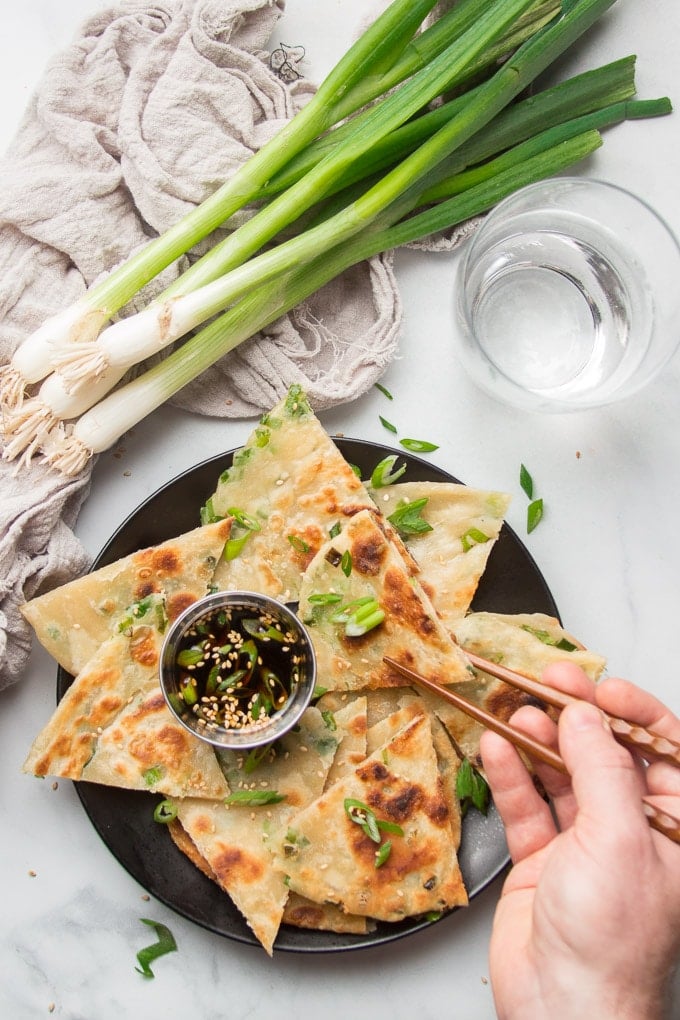 Hand With Chopsticks Removing a Scallion Pancake Slice from a Plate