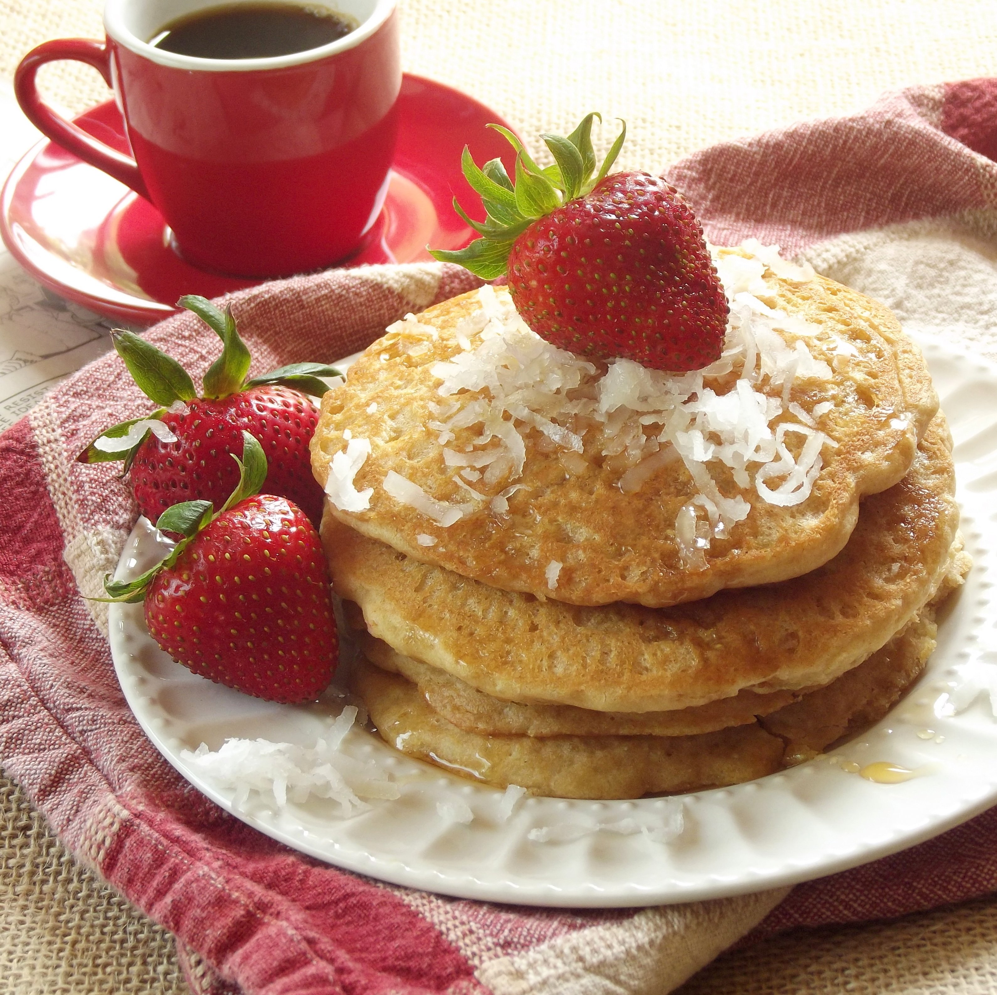 Stack of Quinoa Pancakes and Strawberries on a Plate with Coffee Cup in the Background