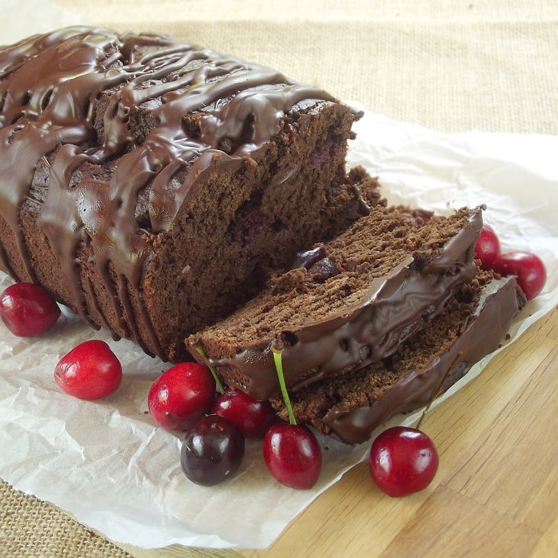 Sliced loaf of Chocolate Cherry Bread on a Cutting Board with Fresh Cherries