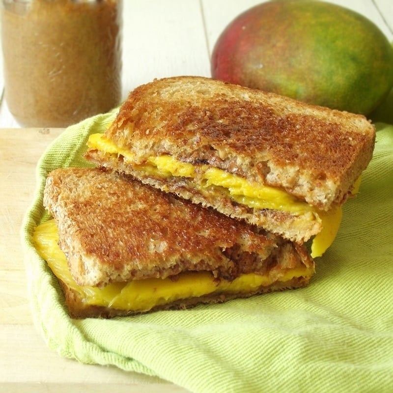 Two Halves of a Grilled Mango Sandwich with Mango and Jar of Almond Butter in the Background