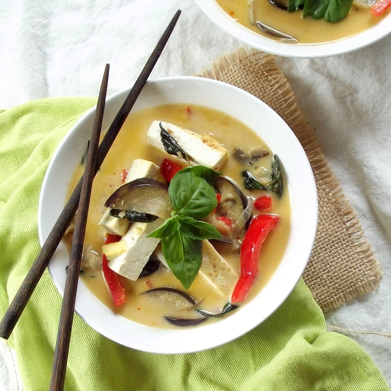 Overhead View of a Bowl of Eggplant Curry with Chopsticks and Basil Leaves on Top