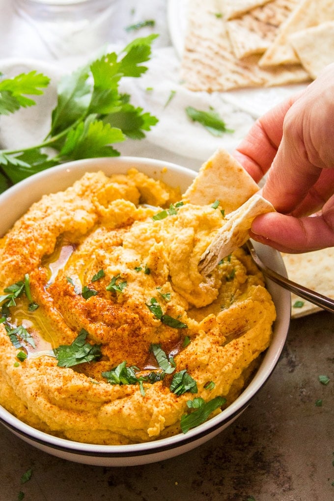 Hand Dipping a Pita Wedge into a Bowl of Butternut Squash Hummus