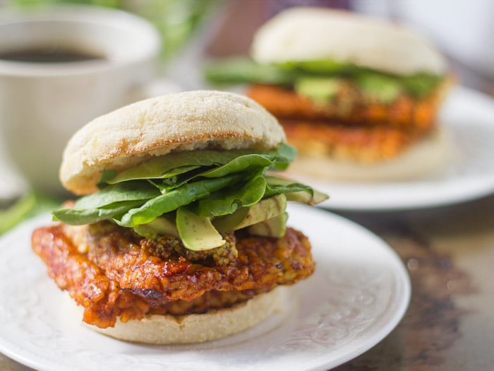 Two Savory Tempeh Breakfast Sandwiches on Plates with Coffee Cup