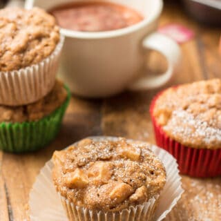 Vegan Apple Cider Muffin with Powdered Sugar on Top, with Tea Cup and Additional Muffins in the Background