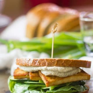 Smoky Baked Tofu Sandwich with Wasabi Cashew Mayo with Drinking Glass, Scallions and Bread in the Background