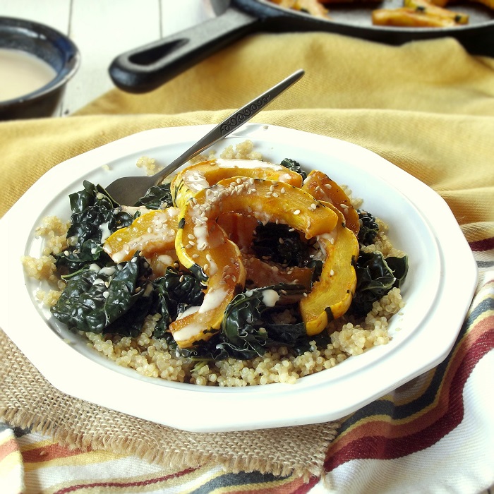 Bowl of Quinoa Topped with Kale and Delicata Squash Sitting on a Yellow Fabric with Skillet in the Background