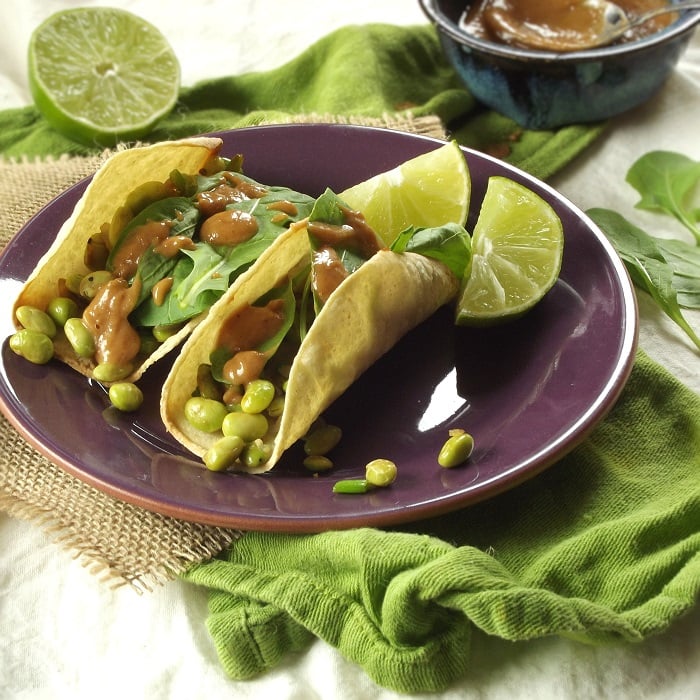 Two Edamame Tacos on a Plate with Lime Slices, Dish of Peanut Sauce in the Background