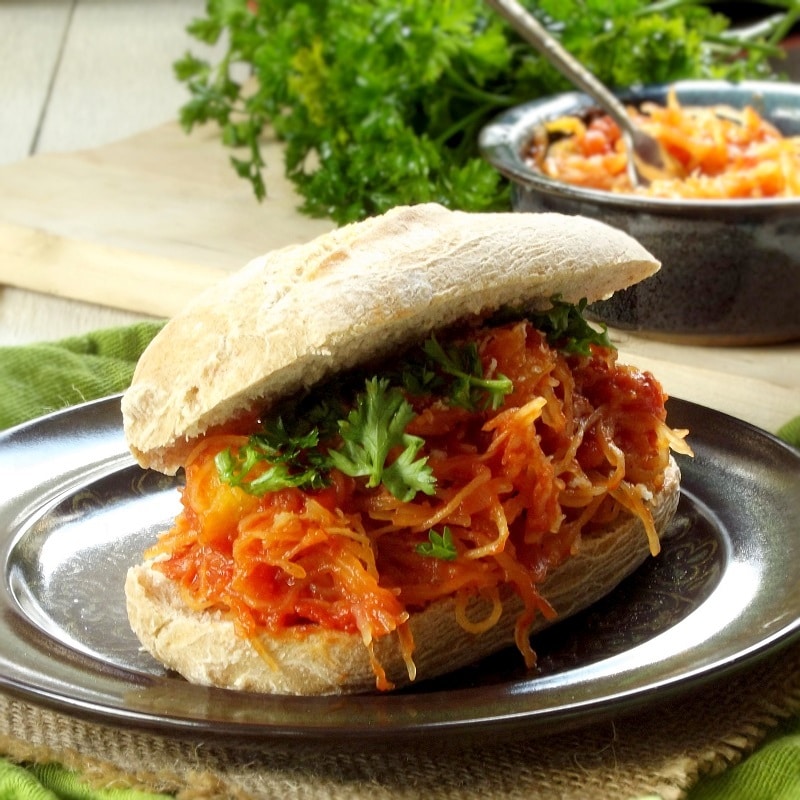 Spaghetti Squash Sandwich on a Plate with Dish of Spaghetti Squash and Bunch of Parsley in the Background