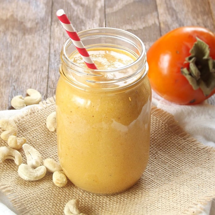 Persimmon Smoothie in a Glass with Fresh Persimmon and Cashews in the Background