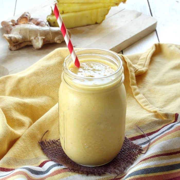 Turmeric Smoothie in a Glass with Ginger and Pineapple Slices in the Background