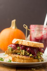 Vegan Thanksgiving Sandwich on a Plate with Pumpkin and Jar of Cranberry Sauce in the Background