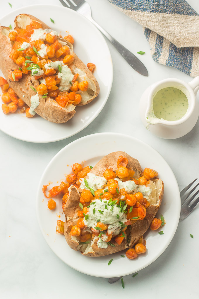 Marble Surface Set with Two Buffalo Chickpea Stuffed Potatoes On Plates, Forks and Container of Ranch Dressing