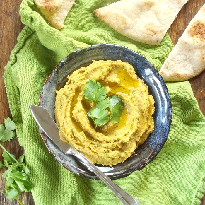 Overhead View of a Bowl of Curry Hummus with Fresh Cilantro and Pita Bread