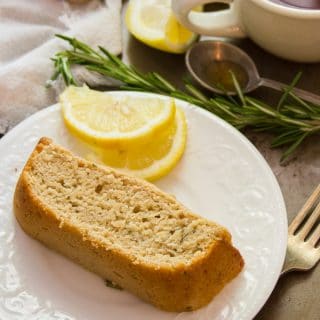 Slice of Rosemary Lemon Vegan Pound Cake on a Plate with Fork, Coffee Cup, Rosemary and Lemon Wedges in the Background