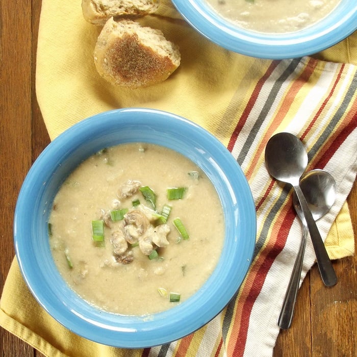 Overhead View of Two Bowls of Cauliflower Mushroom Soup with Bread and Spoons on the Side