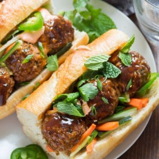 Close Up of a Vegan Meatball Banh Mi on a Plate with Drinking Glass in the Background