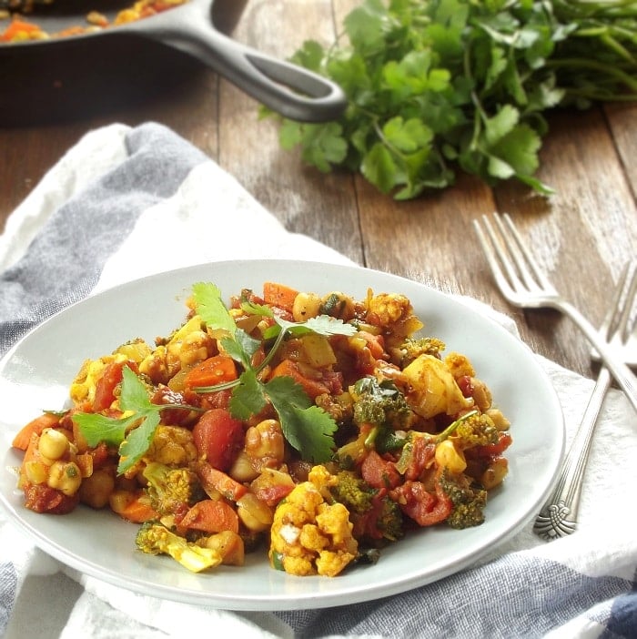 Plate of Veggie Chana Masala with Forks on the Side, Skillet and Bunch of Cilantro in the Background