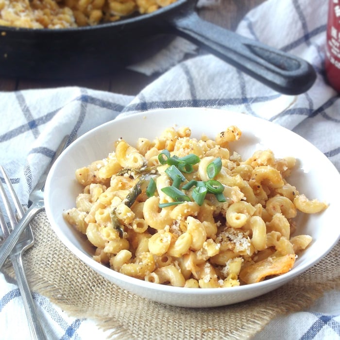 Bowl of Vegan Kimchi Mac and Cheese with Sriracha Bottle and Skillet in the Background