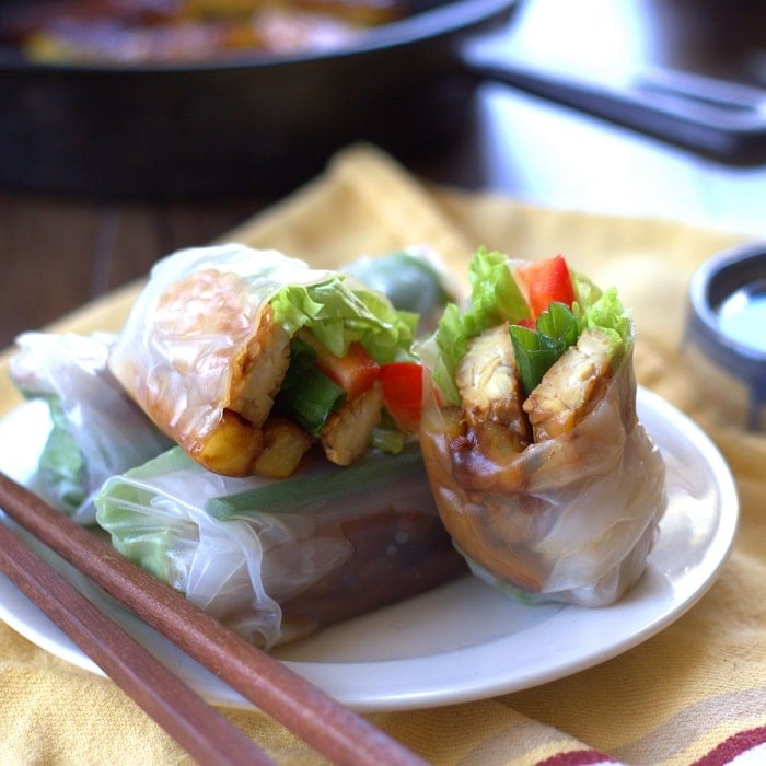 Tempeh Summer Rolls on a Plate with Chopsticks, Skillet and Bowl of Sauce in the Background