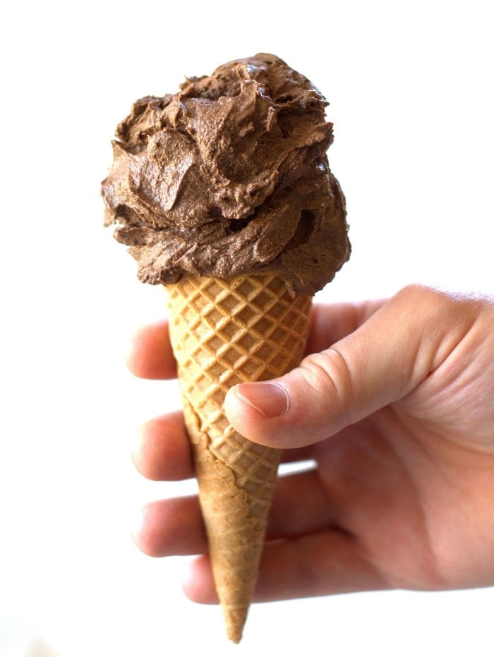 Hand Holding a Vegan Chocolate Ice Cream Cone in Front of a White Background