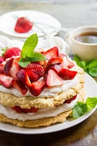 Whole Vegan Strawberry Shortcake on a Plate with Tea Cup and Stack of Dishes in the Background